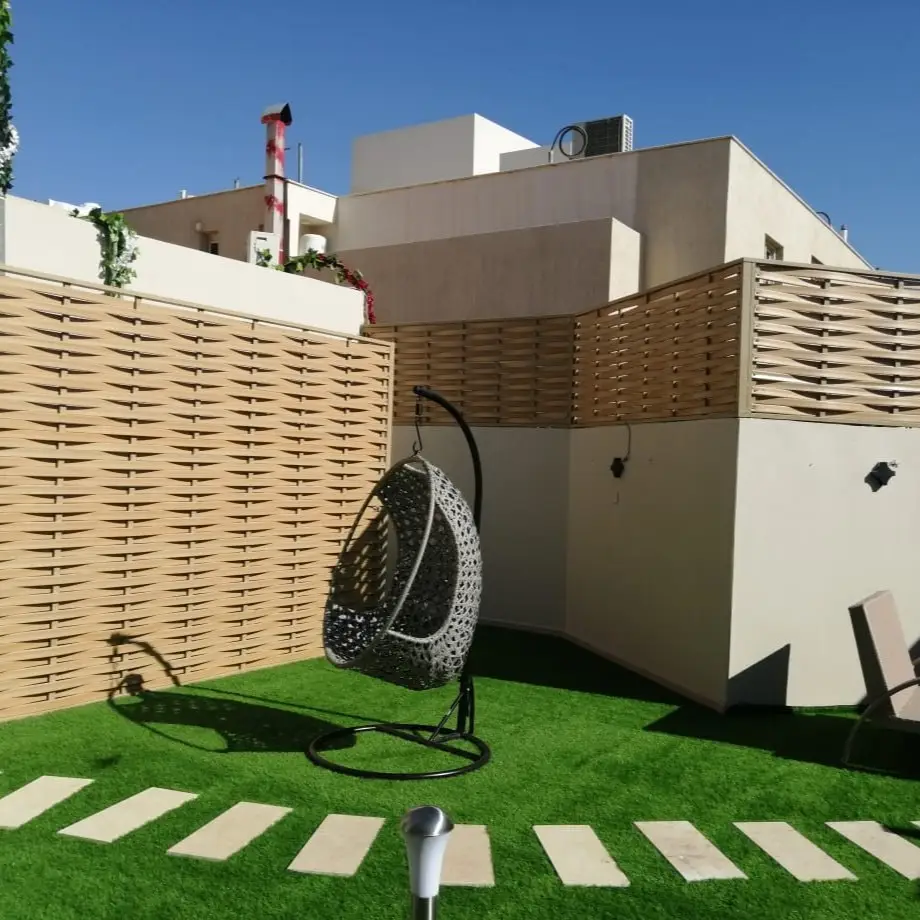 سواتر خشبية أنيقة تحيط بحديقة منزلية في أبها، مع كرسي معلق بتصميم عصري، تعزز من جمال وأناقة المساحة الخارجية وتوفر الخصوصية.